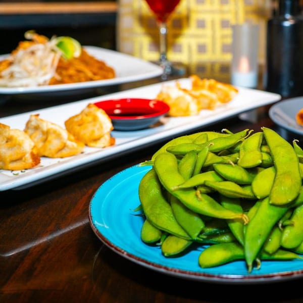 Edamame, dumplings with dipping sauce, and a noodle dish on a dark wooden table.