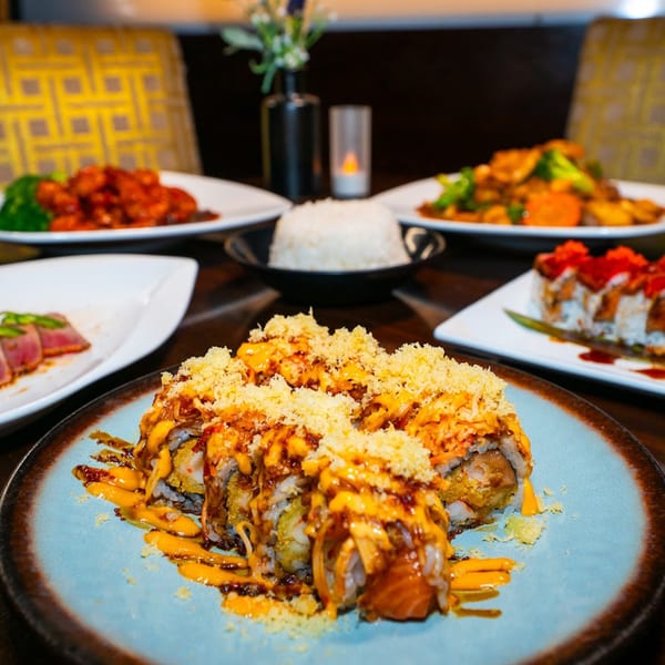 A table laden with various Thai dishes, including sushi rolls, rice, and stir-fries.