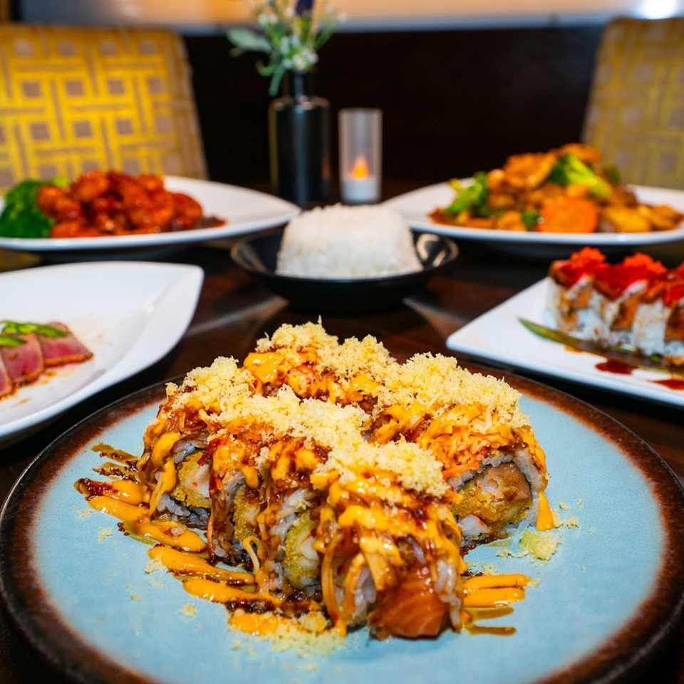 A table laden with various Thai dishes, including sushi rolls, rice, and stir-fries.