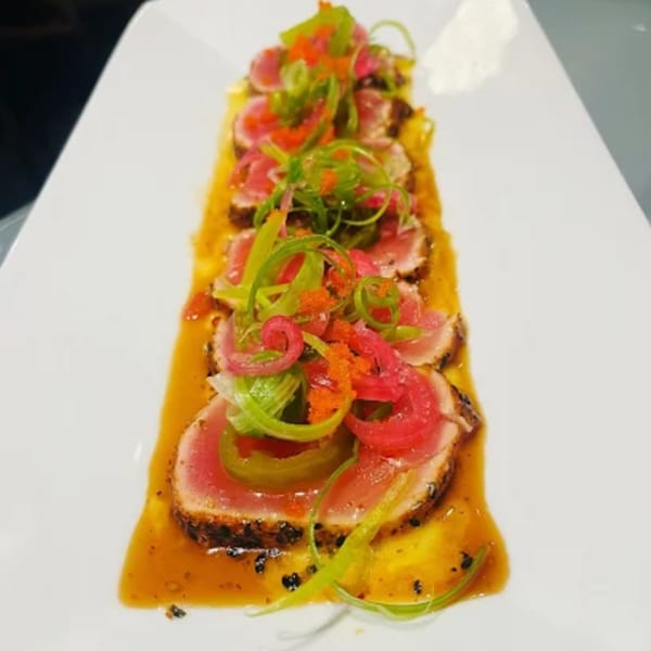 Seared tuna slices with green onions, red onions, and orange roe on a white plate.