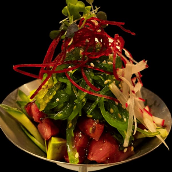 A vibrant Thai salad with tuna, avocado, seaweed, and red radish on a dark background.