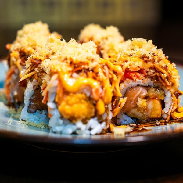Close-up of Made in Asia's sushi rolls, topped with crunchy tempura flakes and drizzled with sauce.